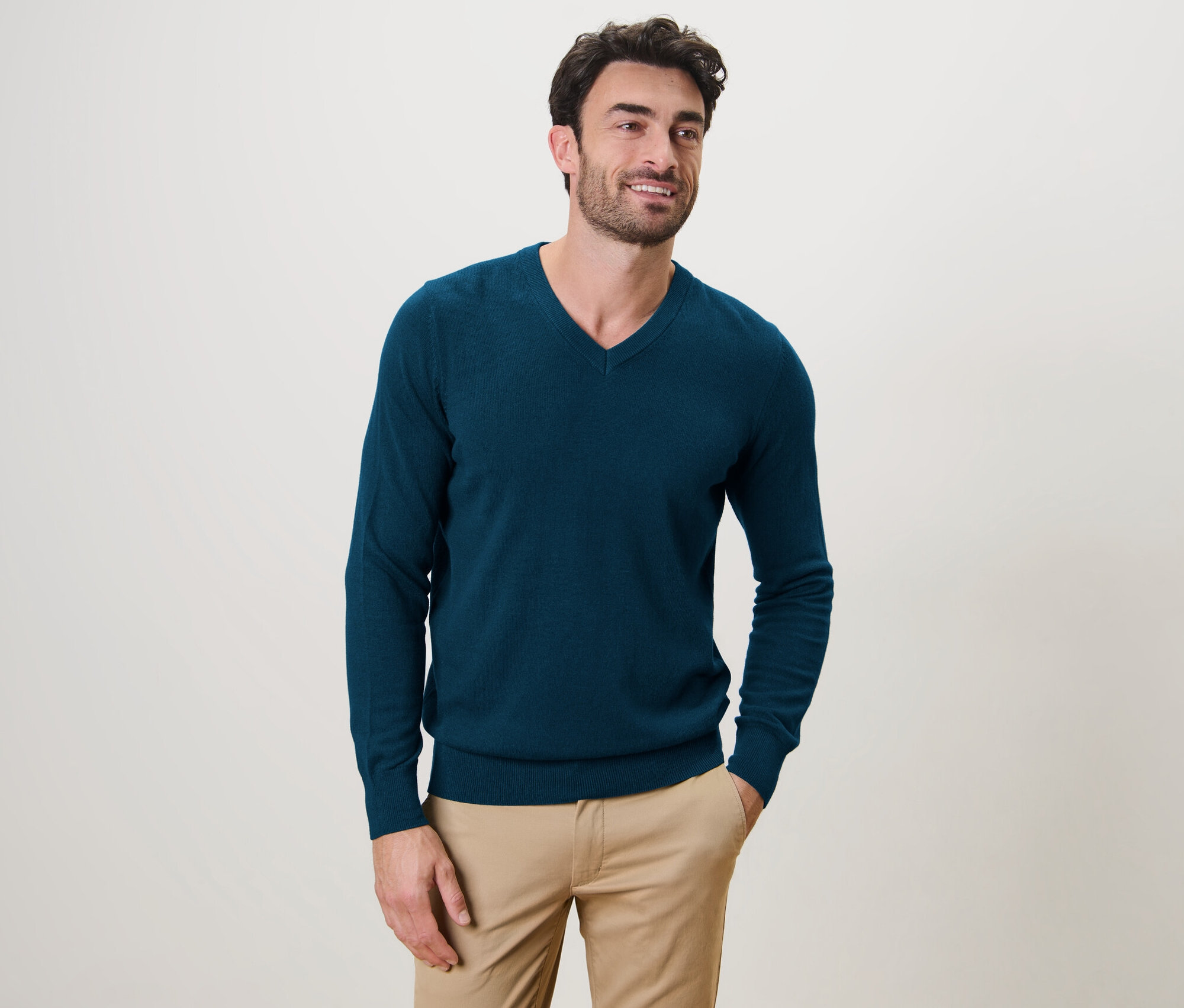 Mann posiert und trägt einen petrolfarbenen Pullover mit V-Ausschnitt.