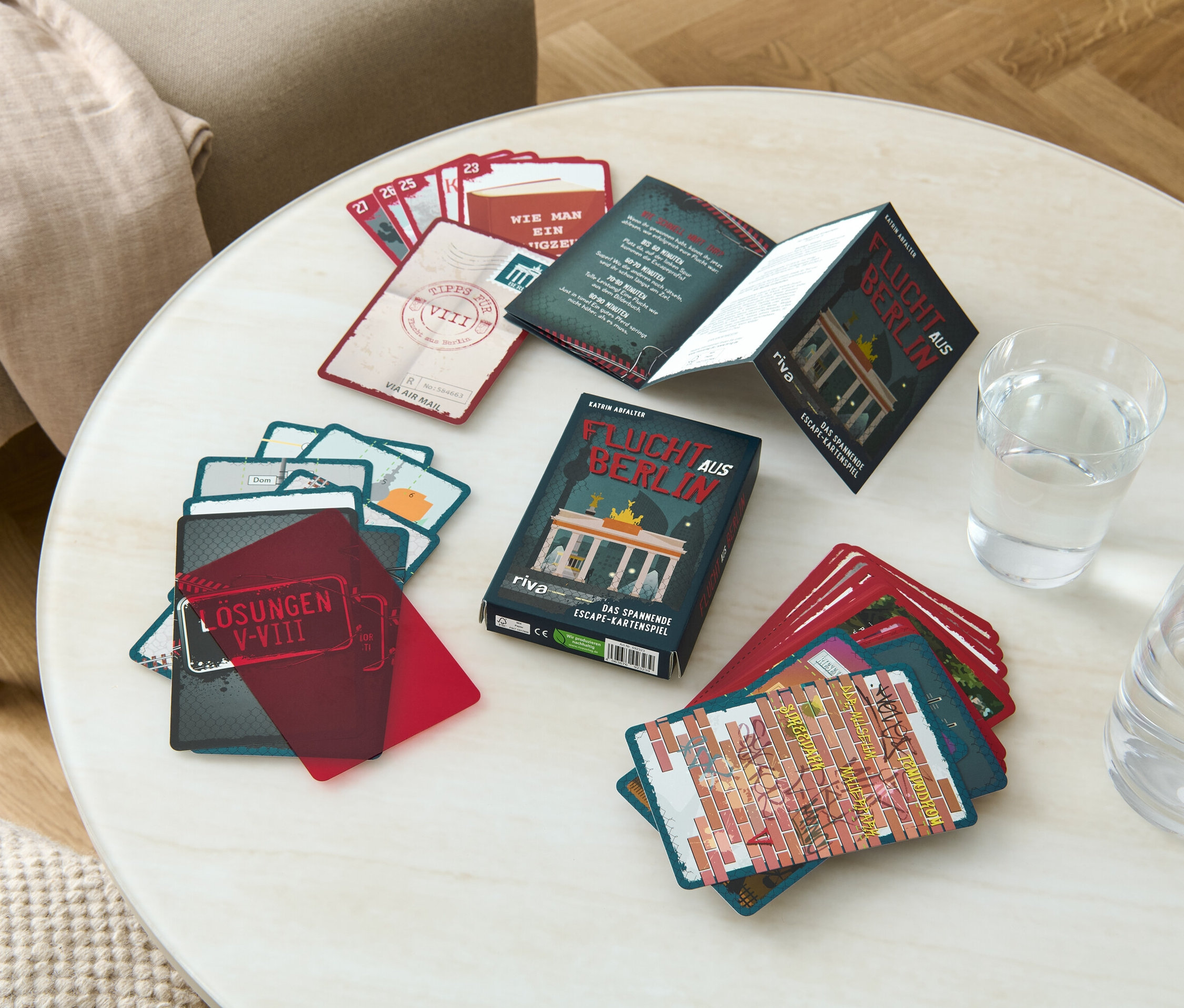 Auf einem Tisch liegen das Escape-Room-Kartenspiel „Flucht aus Berlin“, ein Glas Wasser und eine Karaffe.