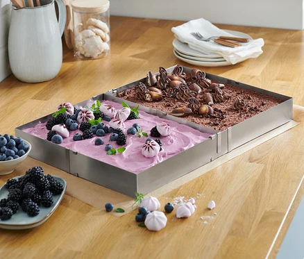 Zwei Edelstahl-Backrahmen mit Obst- und Schokoladenkuchen auf einer Holzplatte.