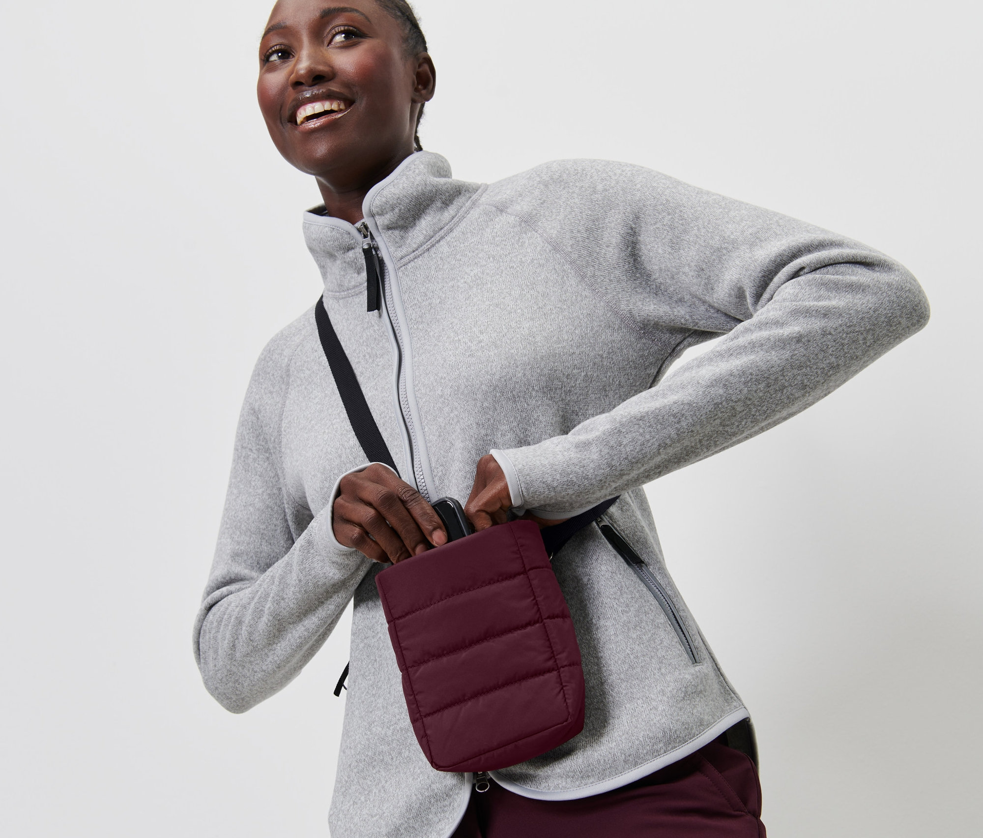 Frau im grauen Fleece legt Smartphone in die isolierte Smartphone-Tasche.