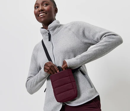 Frau im grauen Fleece legt Smartphone in die isolierte Smartphone-Tasche.