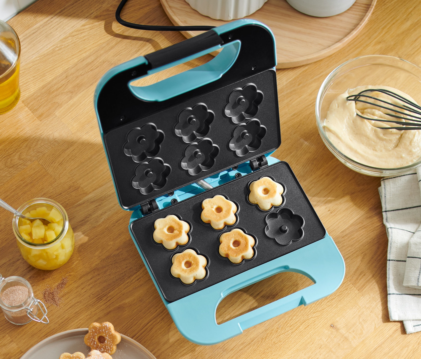 Offenes Waffeleisen, floral, mit Waffeln im Inneren. Waffeln sind auch auf einem Teller.