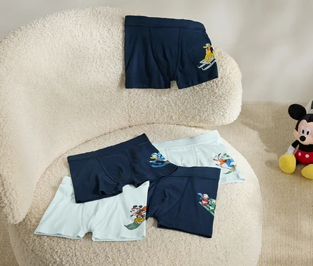 Auf einem beigen Sessel liegen fünf Boxershorts mit Aufdruck. Neben dem Sessel sitzt ein Mickey Mouse Plüschtier mit einem Fußball.