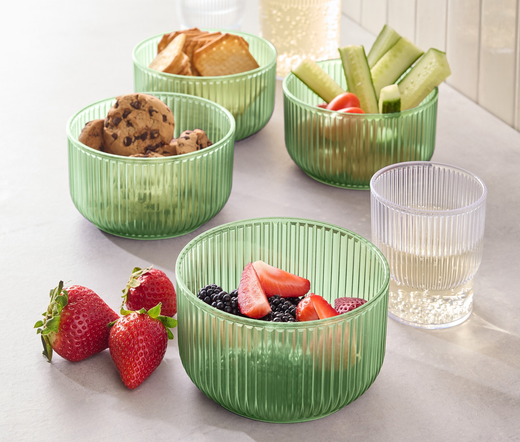 Vier Kunststoff-Schalen gefüllt mit Lebensmitteln, darunter Kekse, Brot, Gurken und Erdbeeren.