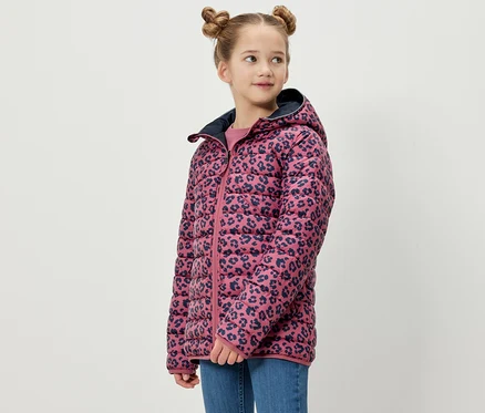Mädchen posiert in einer 2-in-1-Kinder-Softshell- und Steppjacke. Die Jacke hat einen rosafarbenen Hintergrund mit einem marineblauen Tiermuster.