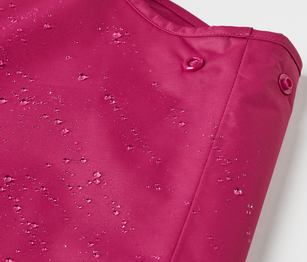 Detailaufnahme einer Kinder-Thermo-Regenhose in Beere mit Wassertropfen.