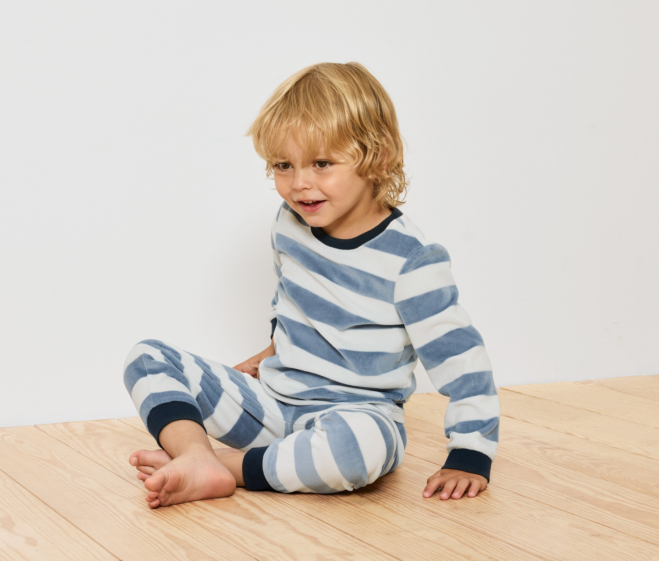 Junge sitzt in gestreiftem Pyjama auf Holzboden.