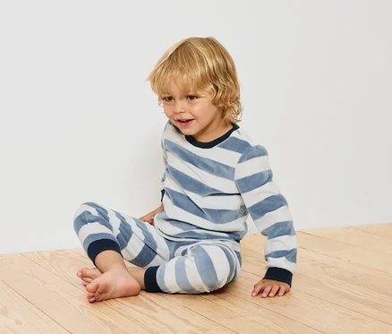 Junge sitzt in gestreiftem Pyjama auf Holzboden.
