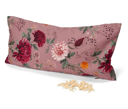 Ein längliches Kissen mit Blumenmuster auf rosa Hintergrund liegt auf einer weißen Fläche neben einem Haufen Füllmaterial.