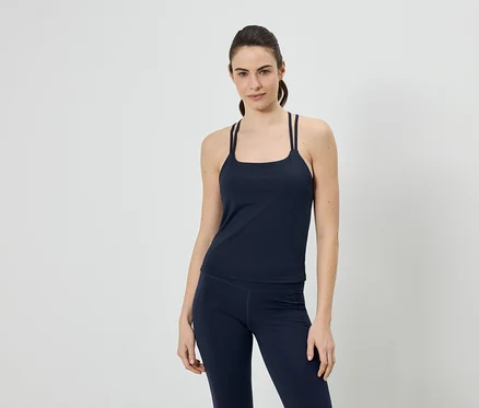 Frau in marineblauem Sporttop mit Trägern und Leggings vor einem neutralen Hintergrund.