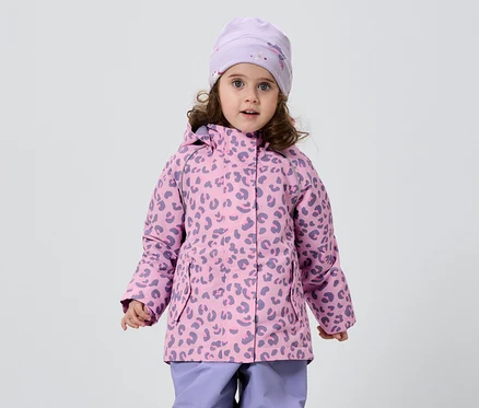 Ein kleines Mädchen mit lockigem Haar trägt eine rosa-lila Jacke mit Leopardenmuster, eine passende Mütze und lila Hosen vor einem weißen Hintergrund.