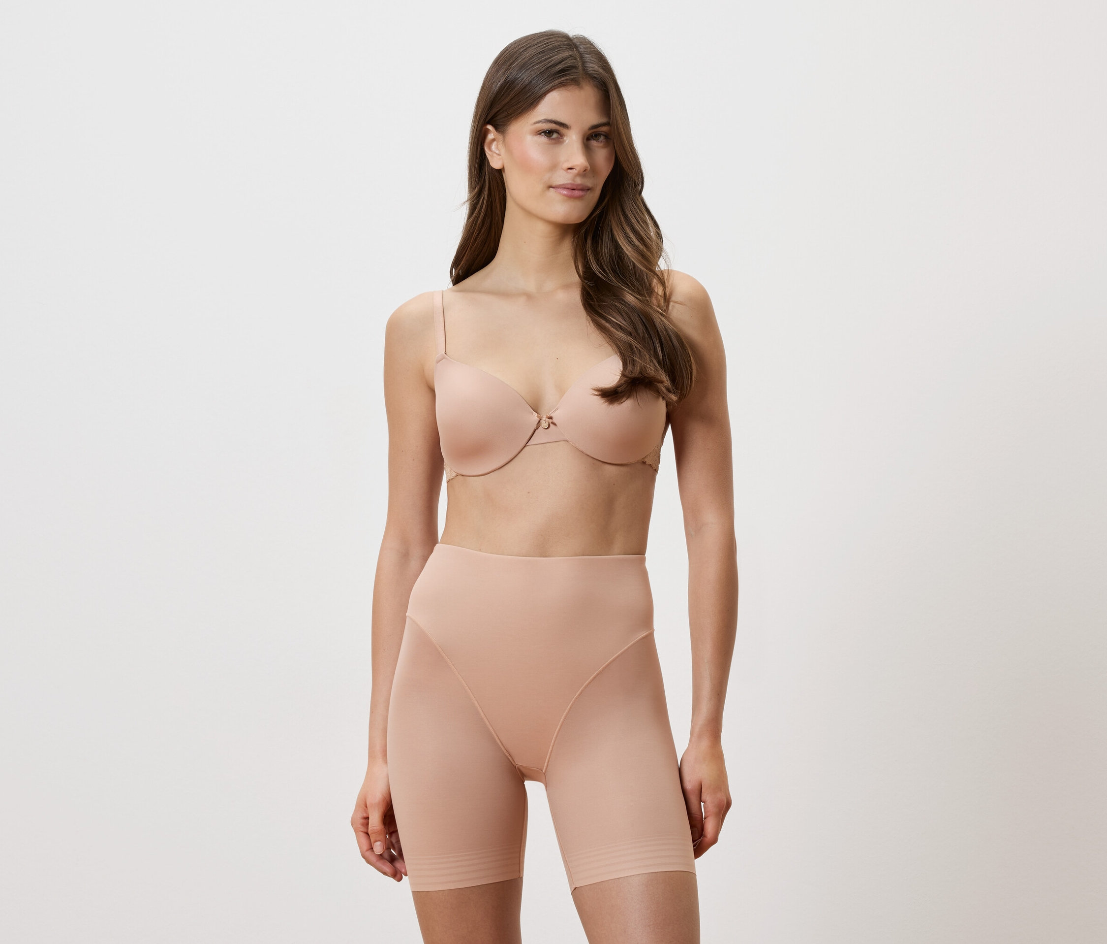 Frau trägt einen hautfarbenen BH und figurformende Shorts vor einem weißen Hintergrund.