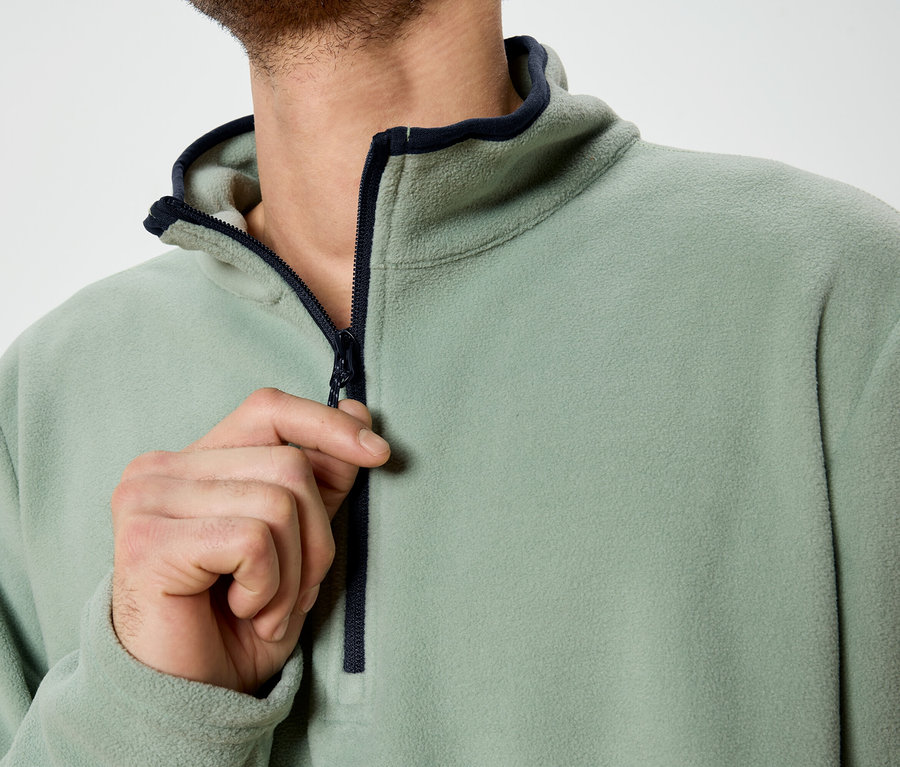 Ein Mann öffnet den Reißverschluss eines hellgrünen Fleece-Pullovers.
