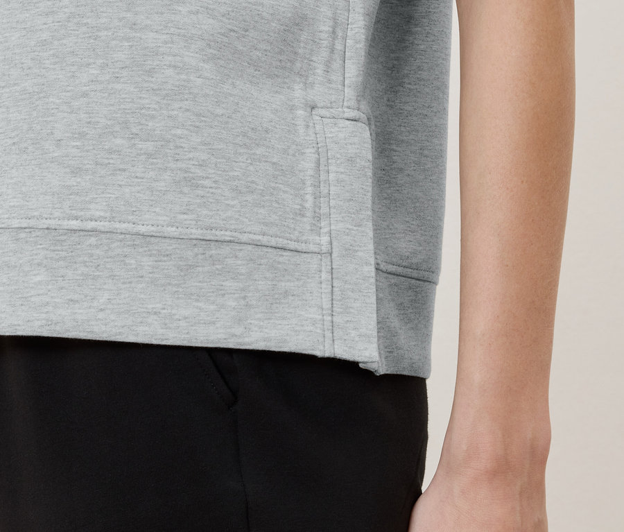 Detailansicht einer Person, die einen hellgrauen Pullover und eine schwarze Hose trägt.