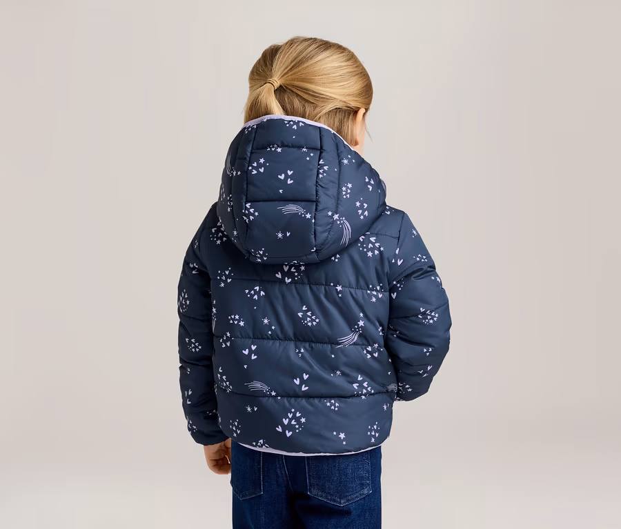 Rückansicht eines Kindes mit blondem Haar, das eine marineblaue Pufferjacke mit Kapuze und Sternschnuppenmuster und Jeans trägt.