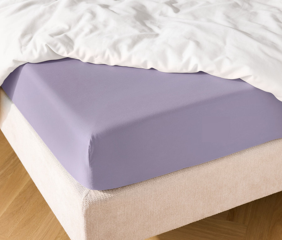 Nahaufnahme eines lila Spannbettlakens auf einem Bett mit einer weißen Bettdecke.