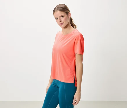 Frau mit Pferdeschwanz trägt ein korallfarbenes T-Shirt und blaue Leggings.