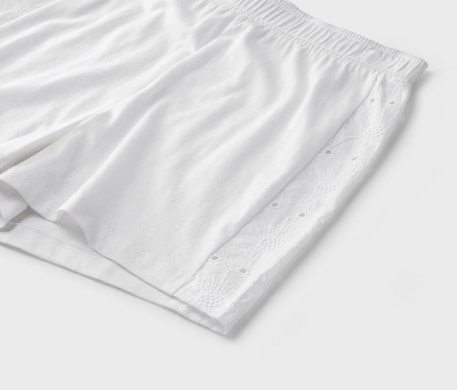 Nahaufnahme von weißen Shorts mit elastischem Bund und Lochstickereidetails an der Seite.
