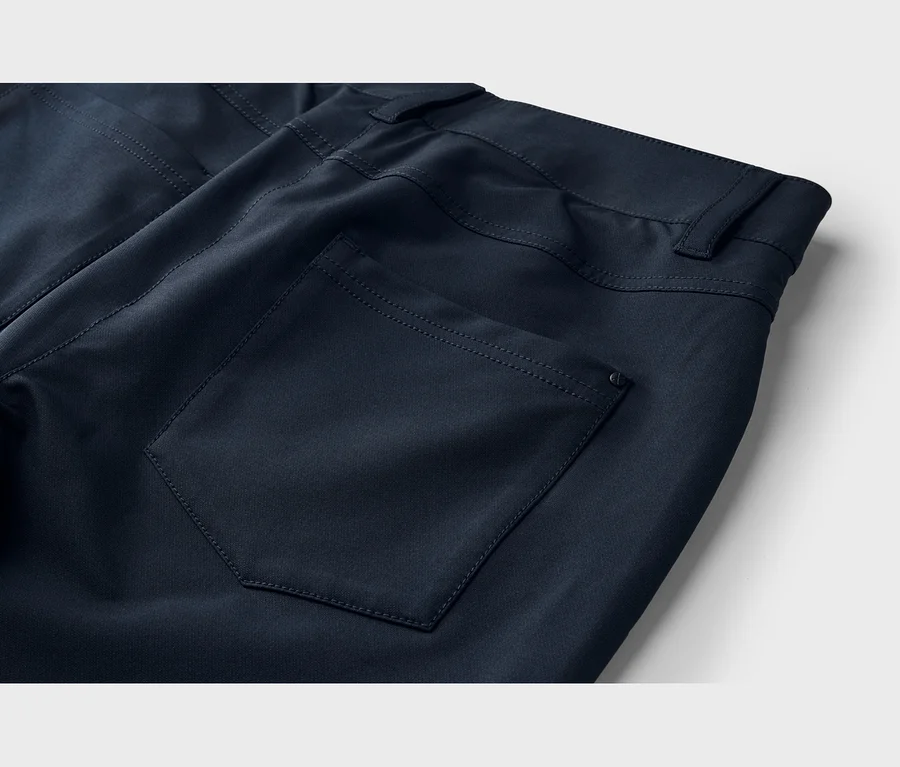 Nahaufnahme der Rückseite einer dunkelblauen Hose mit einer aufgesetzten Gesäßtasche, sichtbaren Nähten, einem kleinen runden Detail und dem Bund mit Gürtelschlaufen.