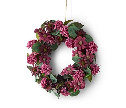 Blumenkranz aus lila und bordeauxroten Blüten und grünen Blättern, an einer Schnur vor weißem Hintergrund hängend.