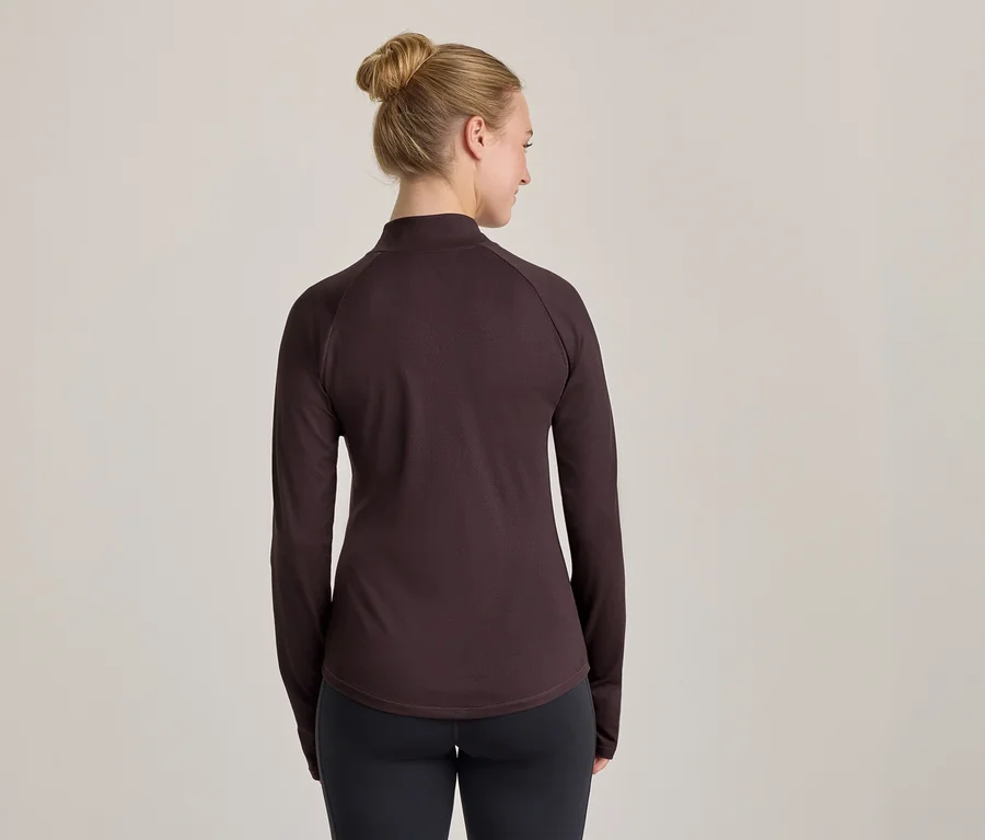 Frau von hinten in einem dunkelbraunen Langarmshirt und schwarzen Leggings, die leicht zur Seite blickt.