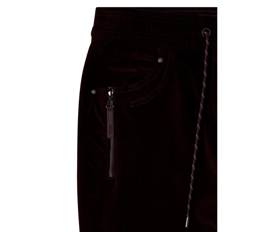 Nahaufnahme einer dunkelroten CECIL Cordhose mit elastischem Bund, einer Reißverschlusstasche mit „CECIL“-Zuglasche und einem Kordelzug mit Metallspitzen.