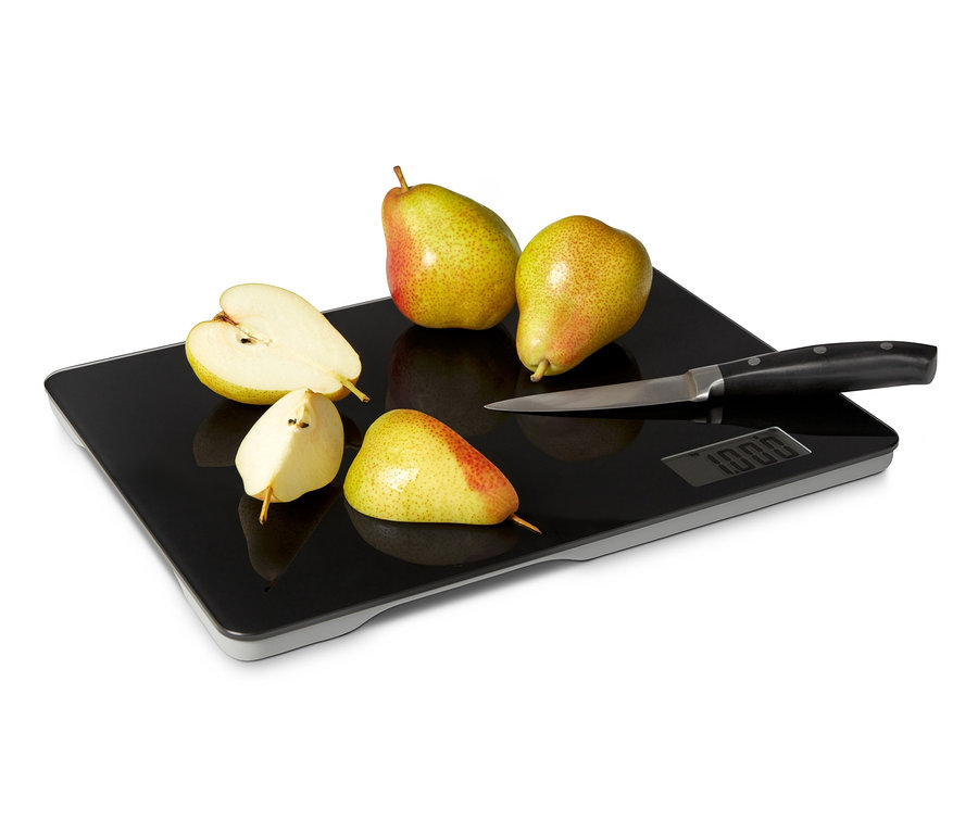 Zwei ganze und zwei halbe Birnen und ein Messer liegen auf einem Schneidebrett mit Küchenwaage.
