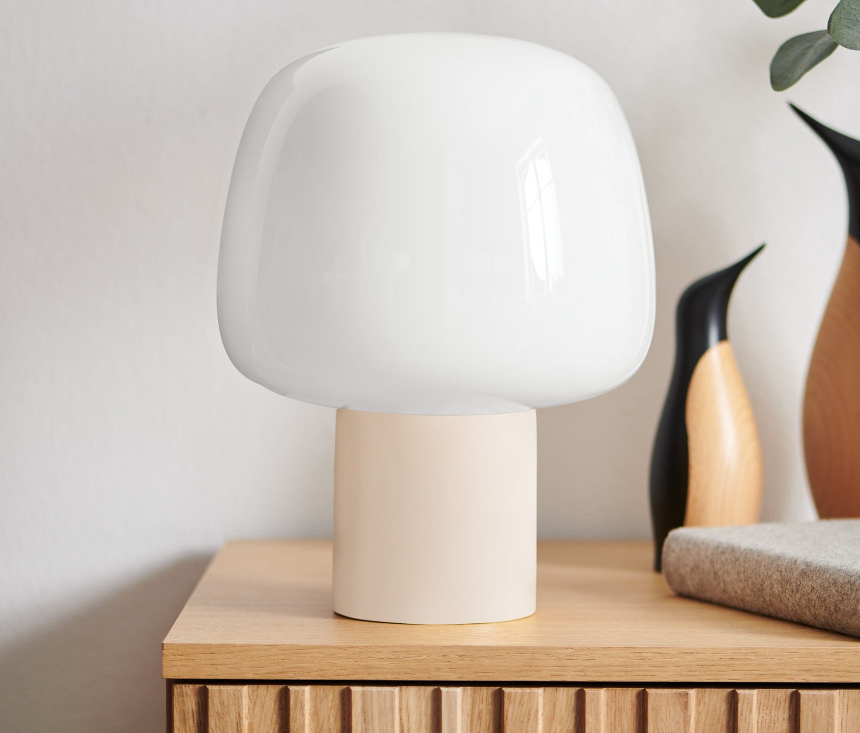 Auf einem Holztisch stehen eine LED-Akku-Tischleuchte, Deko-Objekte und eine Vase mit Pflanzen.