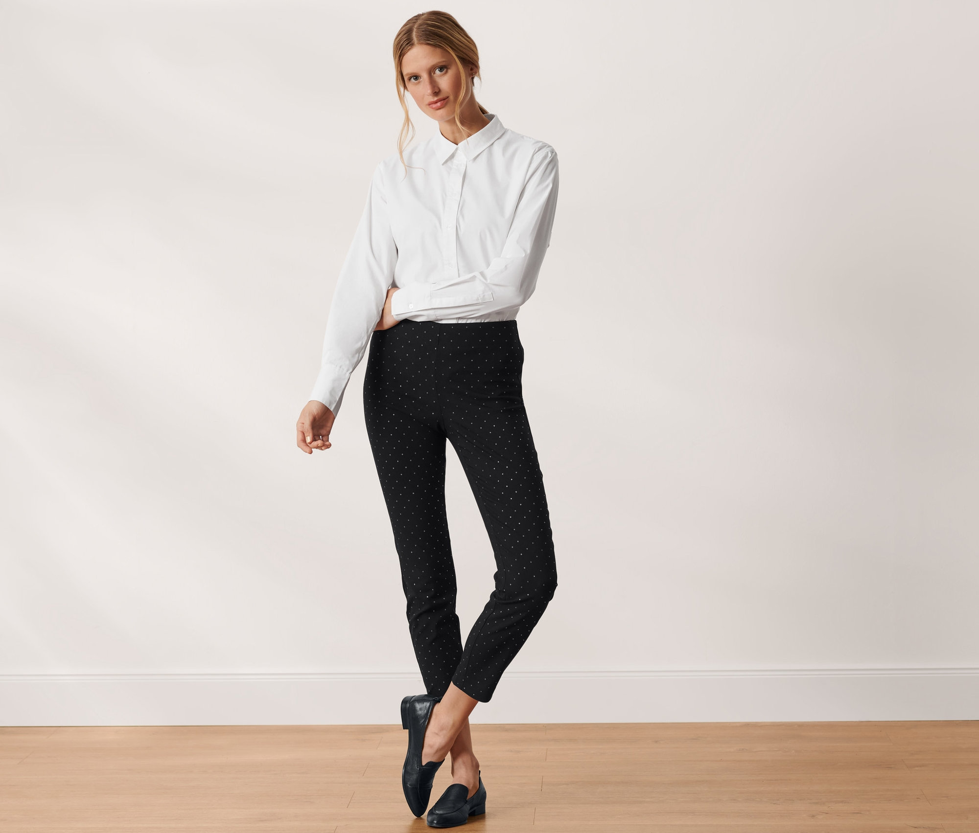 Frau posiert in weißem Hemd und gepunkteter Stretchhose.