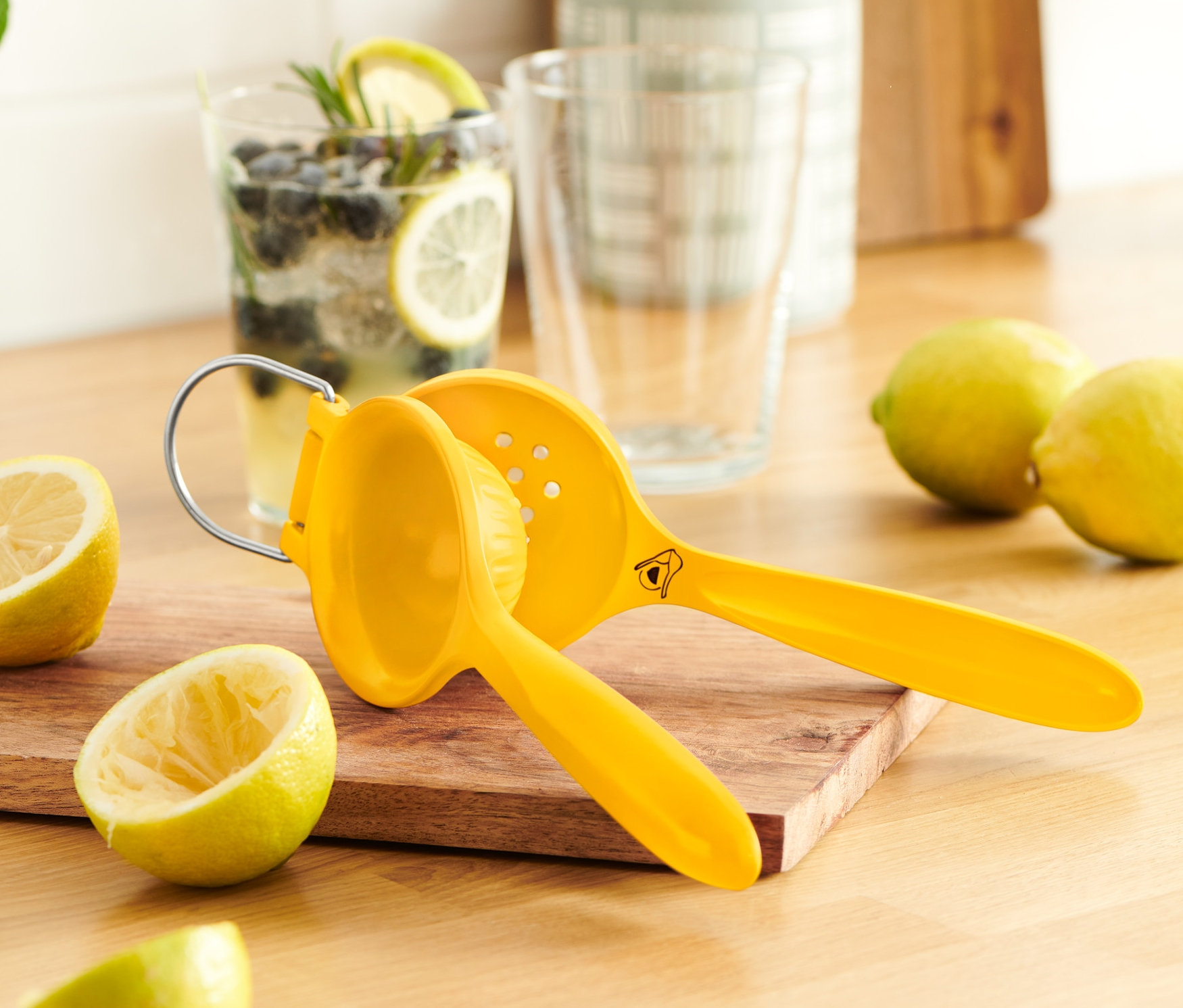 Gelbe Zitruspresse auf Holzbrett neben aufgeschnittenen Zitronen.