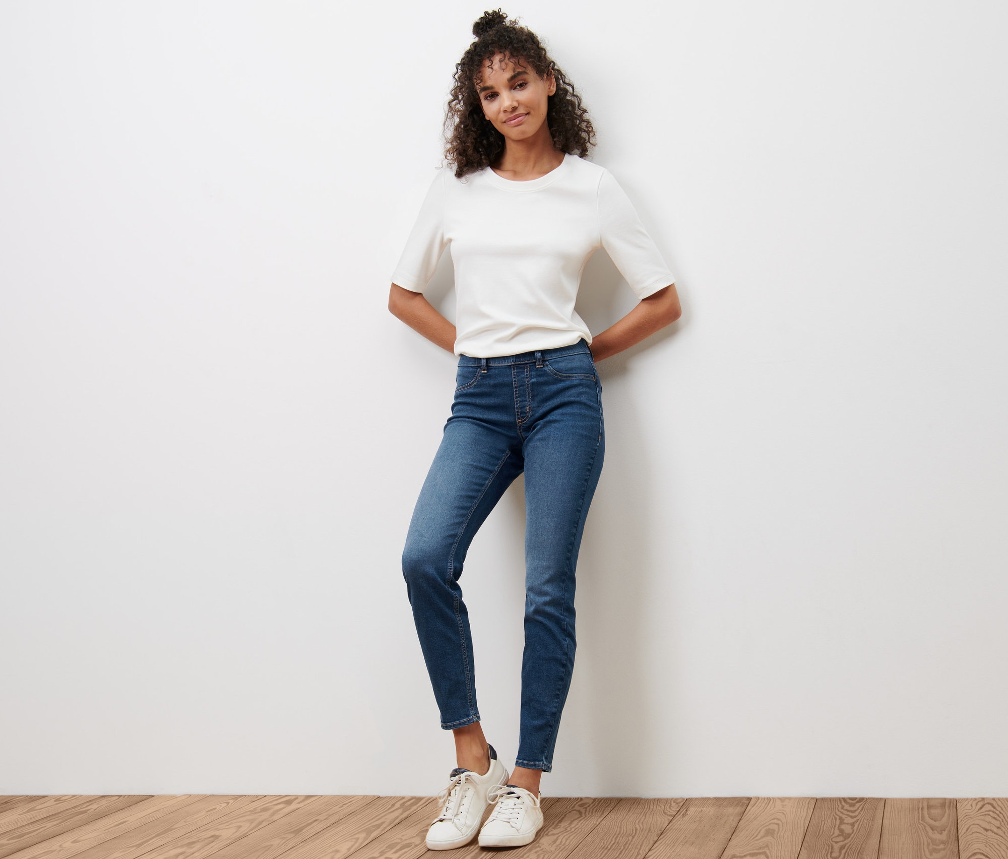 Frau posiert auf Holzboden in blauen Treggings »Fit Nelly« und weißem T-Shirt.