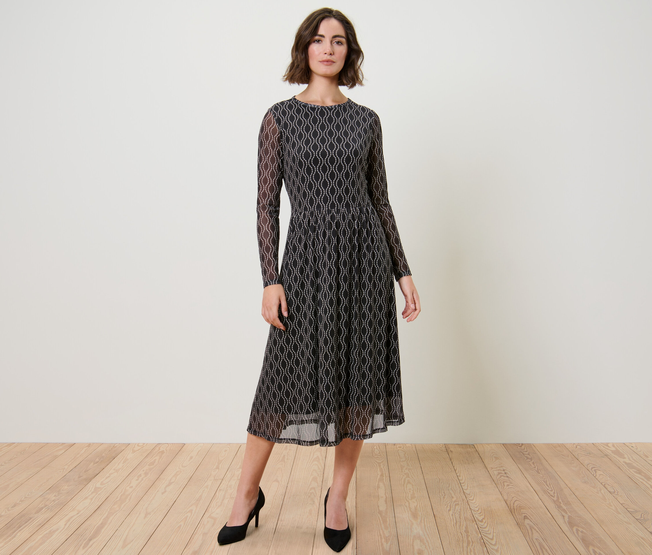 Frau posiert in bedrucktem Mesh-Kleid und schwarzen Pumps.