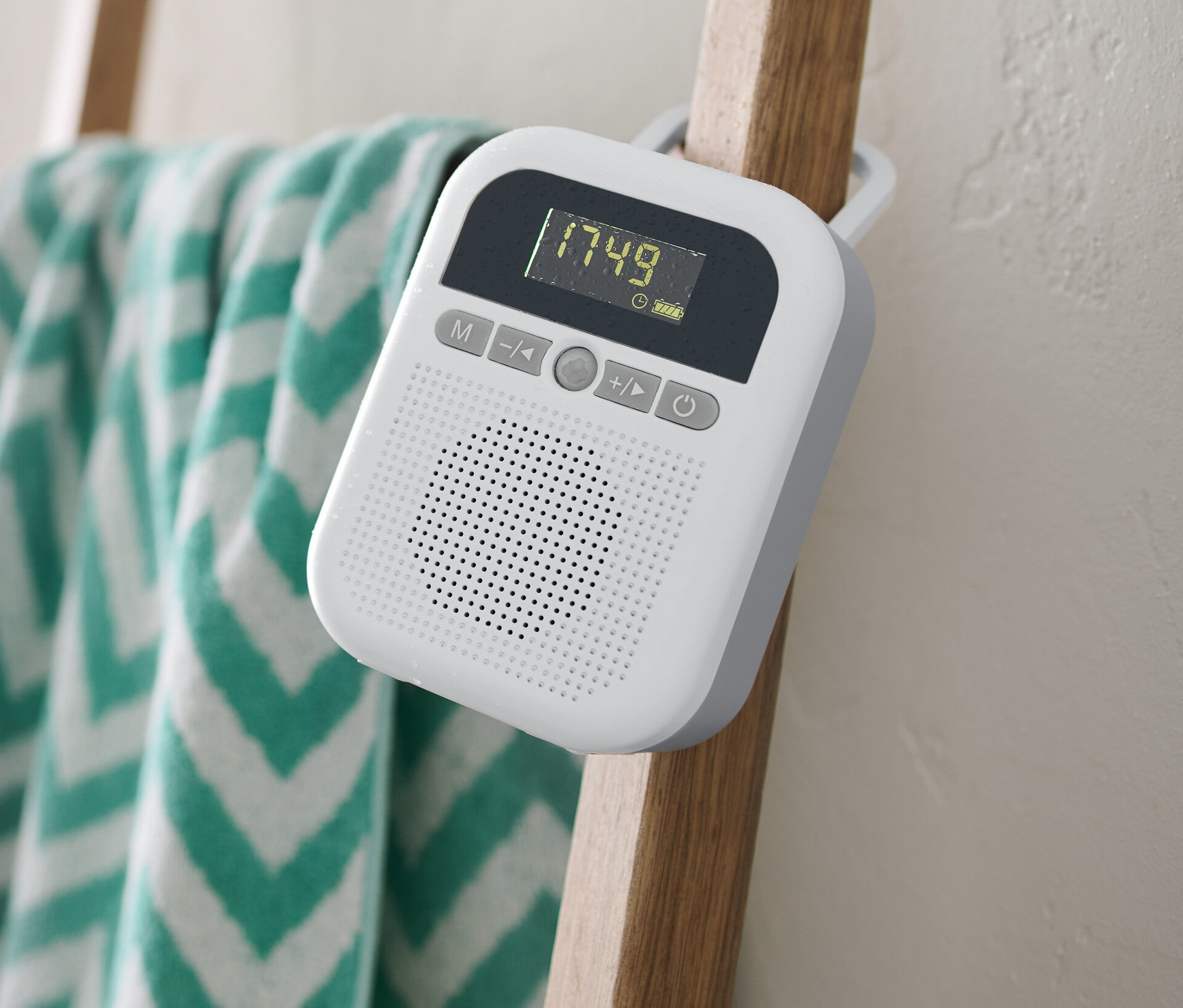 Ein weißes Badradio hängt an einer Holzleiter, an der ein Handtuch hängt.
