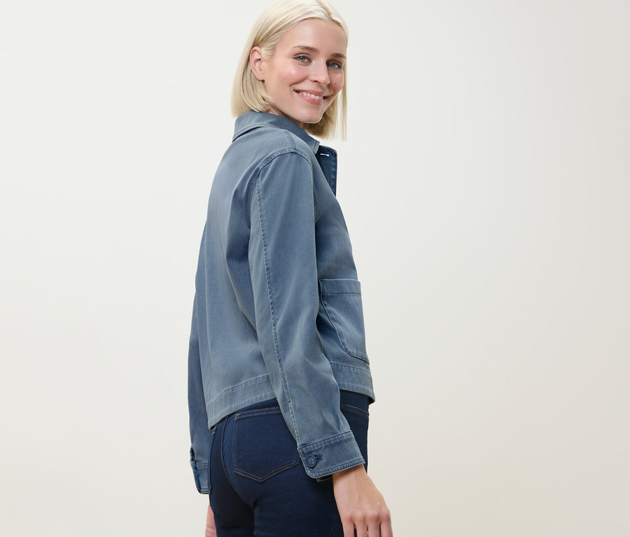 Frau blickt über die Schulter und trägt eine Jerseyjacke in Jeansoptik.