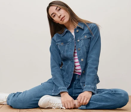 Frau sitzt auf dem Boden und trägt eine Jeansjacke.