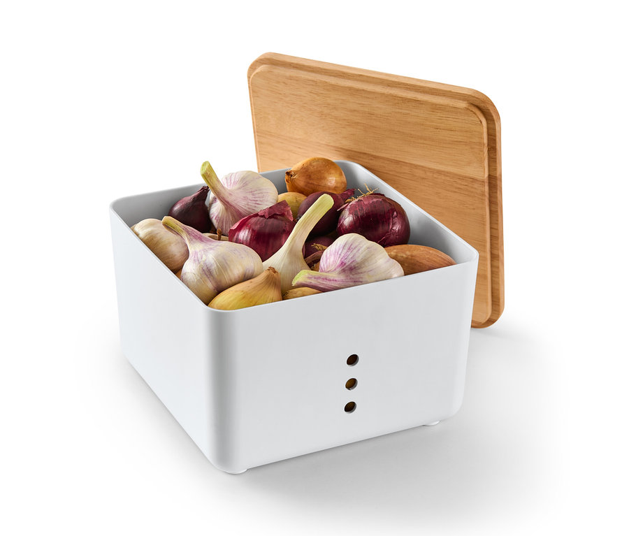 Weißer Aufbewahrungskasten gefüllt mit Zwiebeln und Knoblauch, mit einem hölzernen Deckel, der dagegen gelehnt ist.