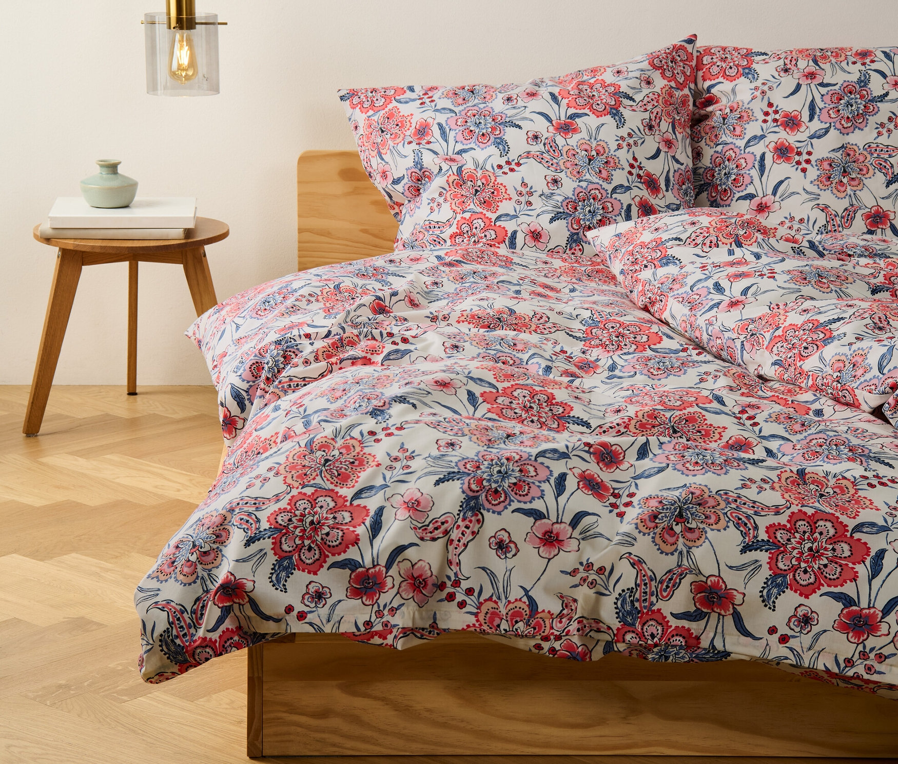 Detailansicht von creme farbener Renforcé-Bettwäsche in Übergröße und Normalgröße mit Blumenmuster auf einem Bett.