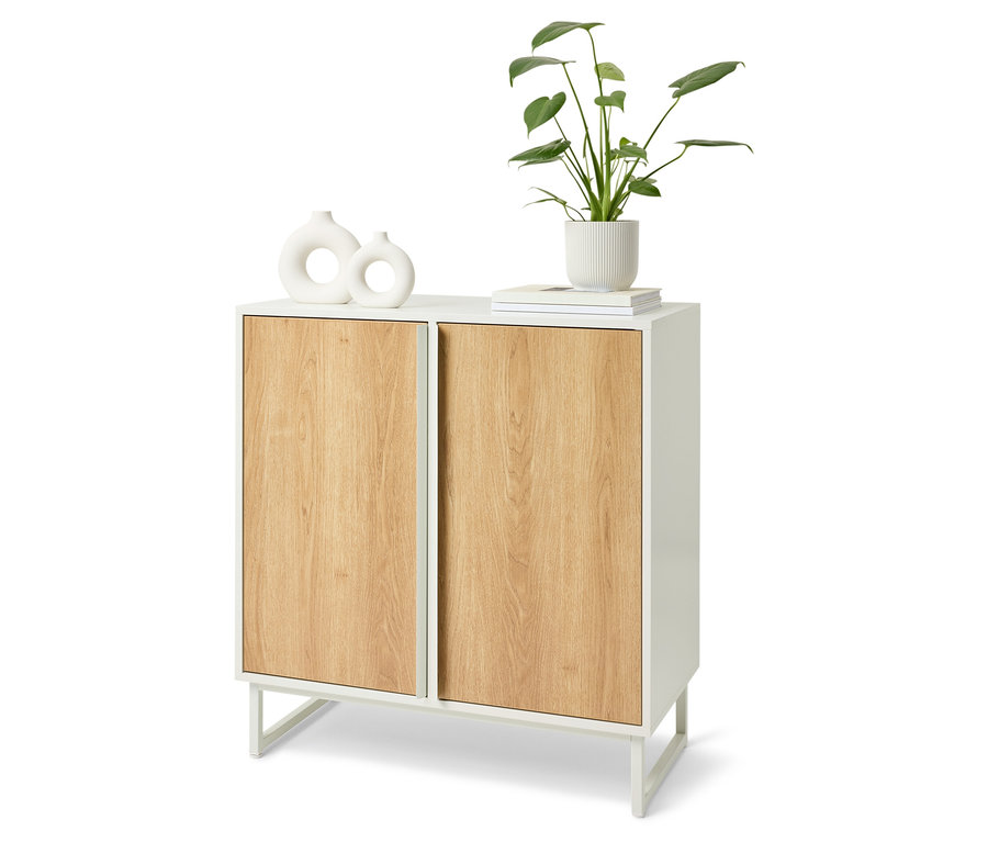 Weißer Schrank mit Holztüren. Auf der Oberseite des Schranks befinden sich zwei weiße Vasen, ein Buch und eine Pflanze in einem weißen Topf.