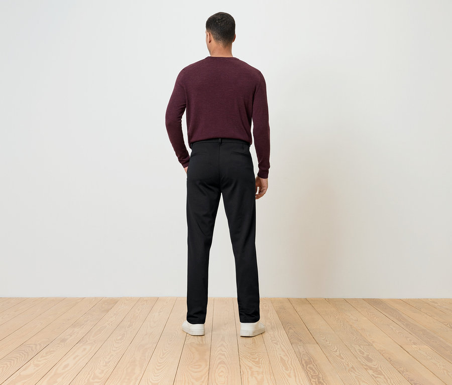 Ein Mann mit dem Rücken zur Kamera trägt einen weinroten Pullover und eine schwarze Hose.