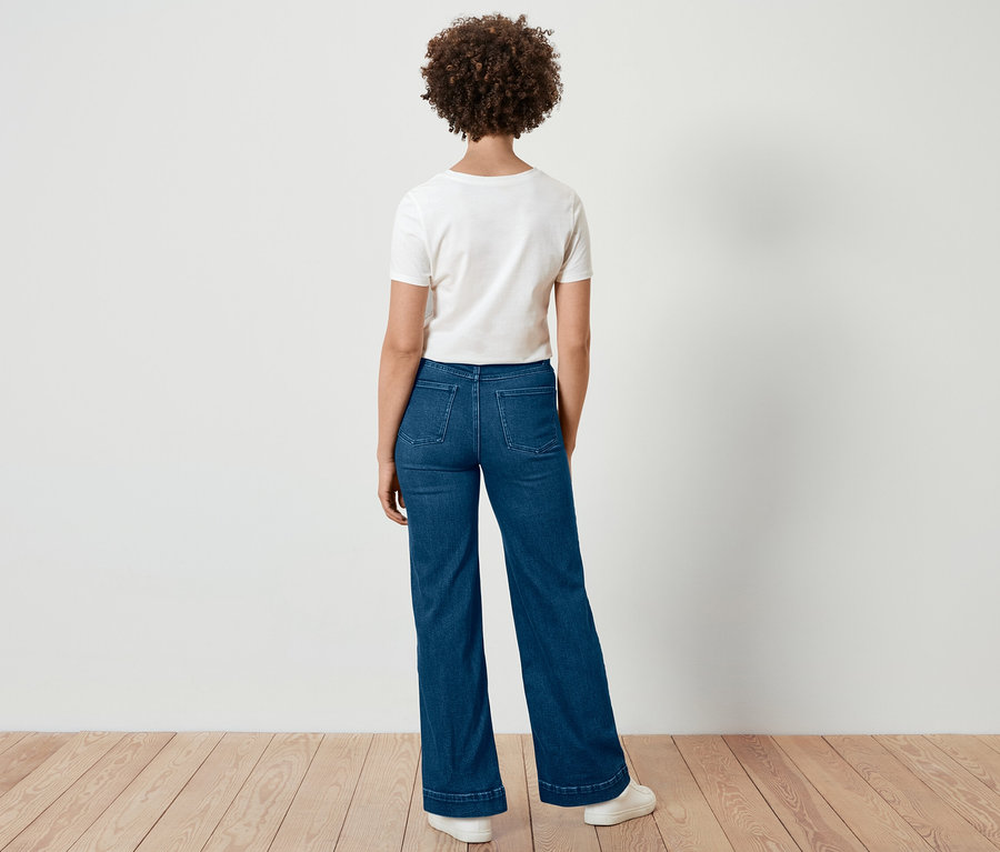 Eine Frau mit lockigem Haar steht mit dem Rücken zur Kamera und trägt eine Wide Leg Jeans – Fit »Viki« und ein weißes T-Shirt.