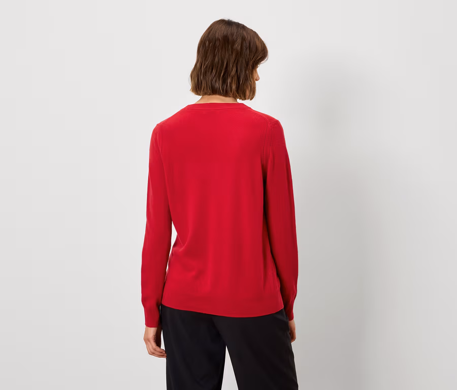 Von hinten ist eine Frau mit kurzen braunen Haaren in einem roten Pullover und einer schwarzen Hose zu sehen.