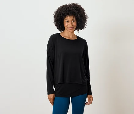 Frau mit Afro-Frisur posiert in einem schwarzen, langärmligen Oberteil und blauen Leggings.