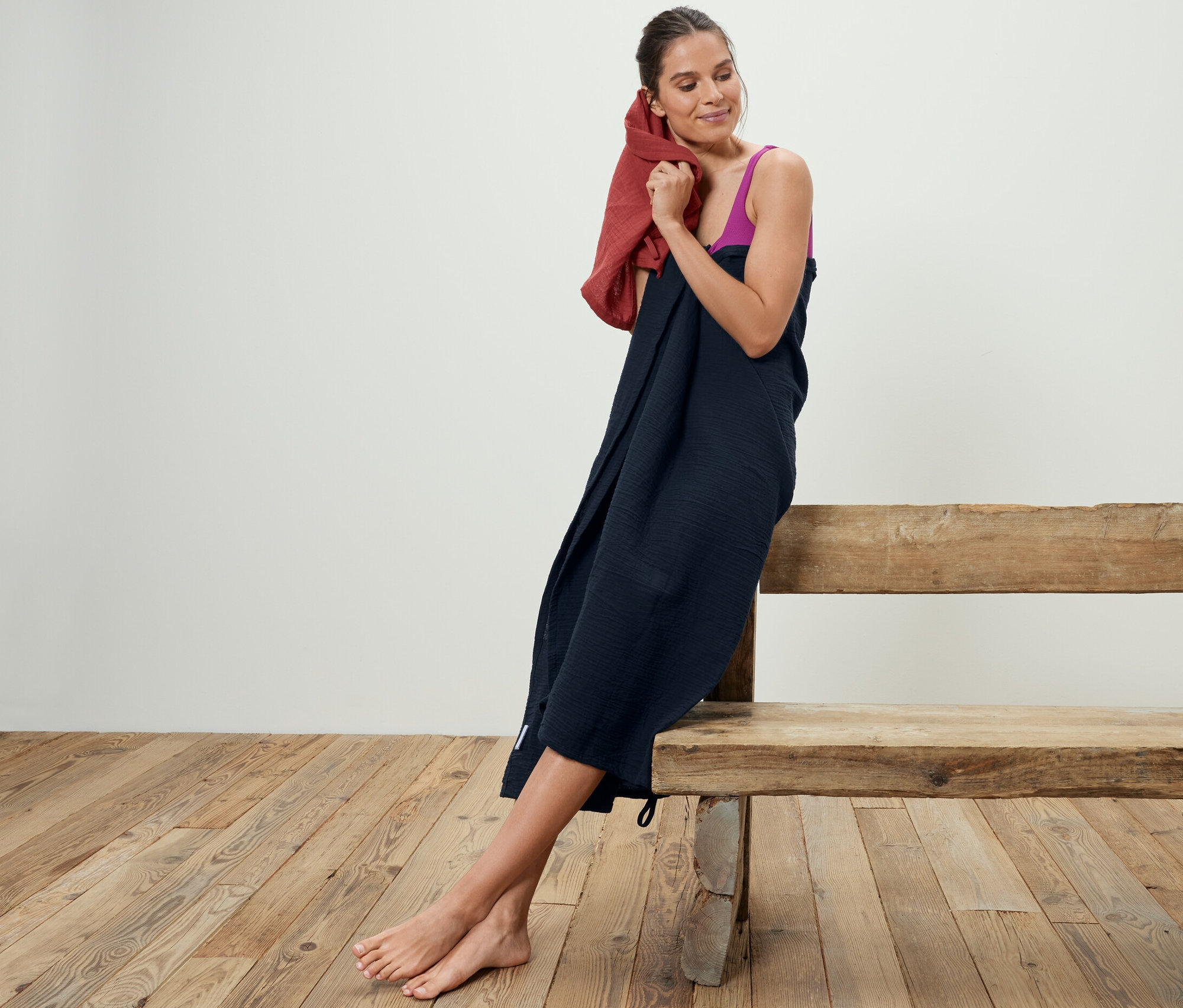 Frau trocknet ihre Haare mit 2 Musselin-Handtüchern, während sie auf einer Holzbank sitzt.