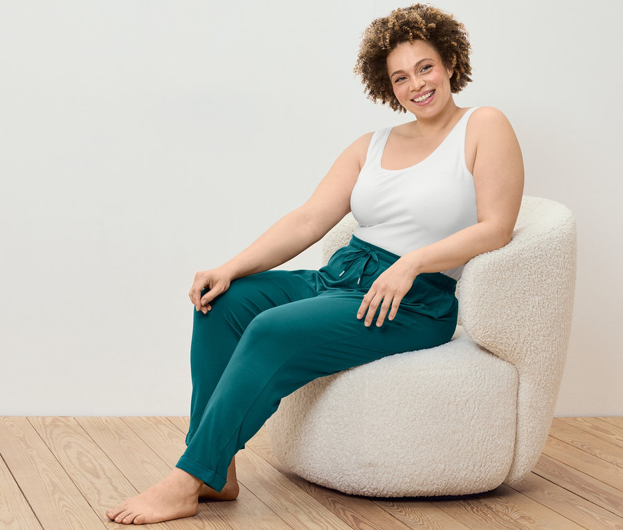 Frau sitzt im Sessel und trägt ein 2 Hemdchen und eine Pyjamahose.