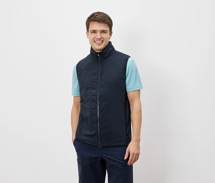 Ein Mann lächelt in die Kamera und trägt eine marineblaue Weste über einem hellblauen T-Shirt.