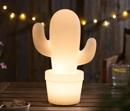 Leuchtender Kaktus in einem Topf auf einem Holztisch, im Hintergrund Lichterkette.