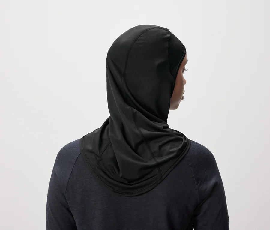 Rückansicht einer Frau mit schwarzem Hijab und dunkelblauem Oberteil vor einem weißen Hintergrund.