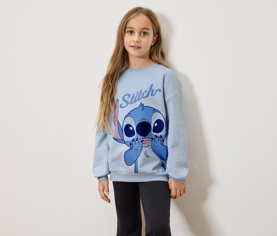 Mädchen mit langen blonden Haaren trägt ein hellblaues Sweatshirt mit Stitch-Druck und schwarze Leggings.