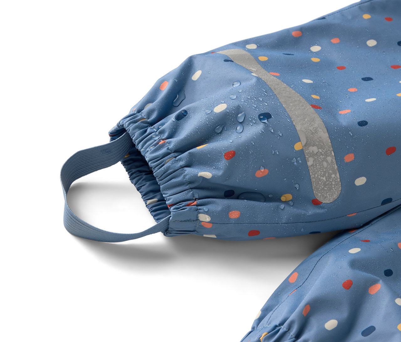 Nahaufnahme eines blauen Regenanzugs mit bunten Punkten und reflektierendem Streifen, auf dem Wassertropfen zu sehen sind.