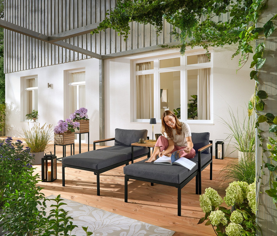 Frau sitzt auf einer grauen Gartenliege und liest ein Buch. Im Hintergrund sind zwei „Elin“ Pflanzsäulen zu sehen.
